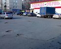 На площади между трёх сетевых магазинов - открытая парковка для покупателей. Дорожное покрытие проездов к парковке со всех трёх сторон - во множестве ям.