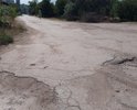 Разбитая дорога по ул. Десантников в пгт. Приморский. Старый асфальт, ямы. Отсутствует освещение и ливневая канализация. Также в плохом состоянии тротуар.